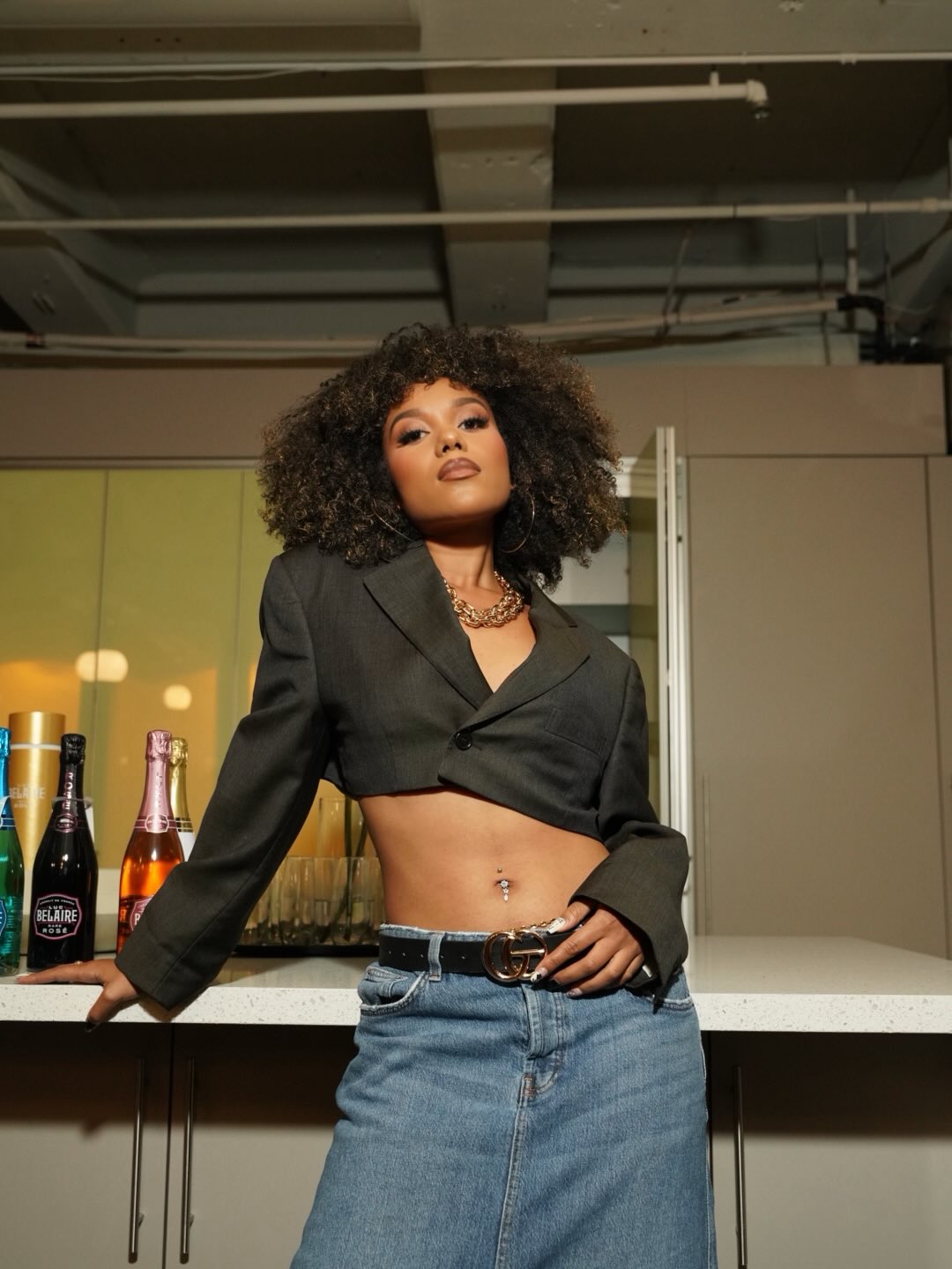 CHIZUKO wearing a cropped charcoal blazer and jeans beside a counter.