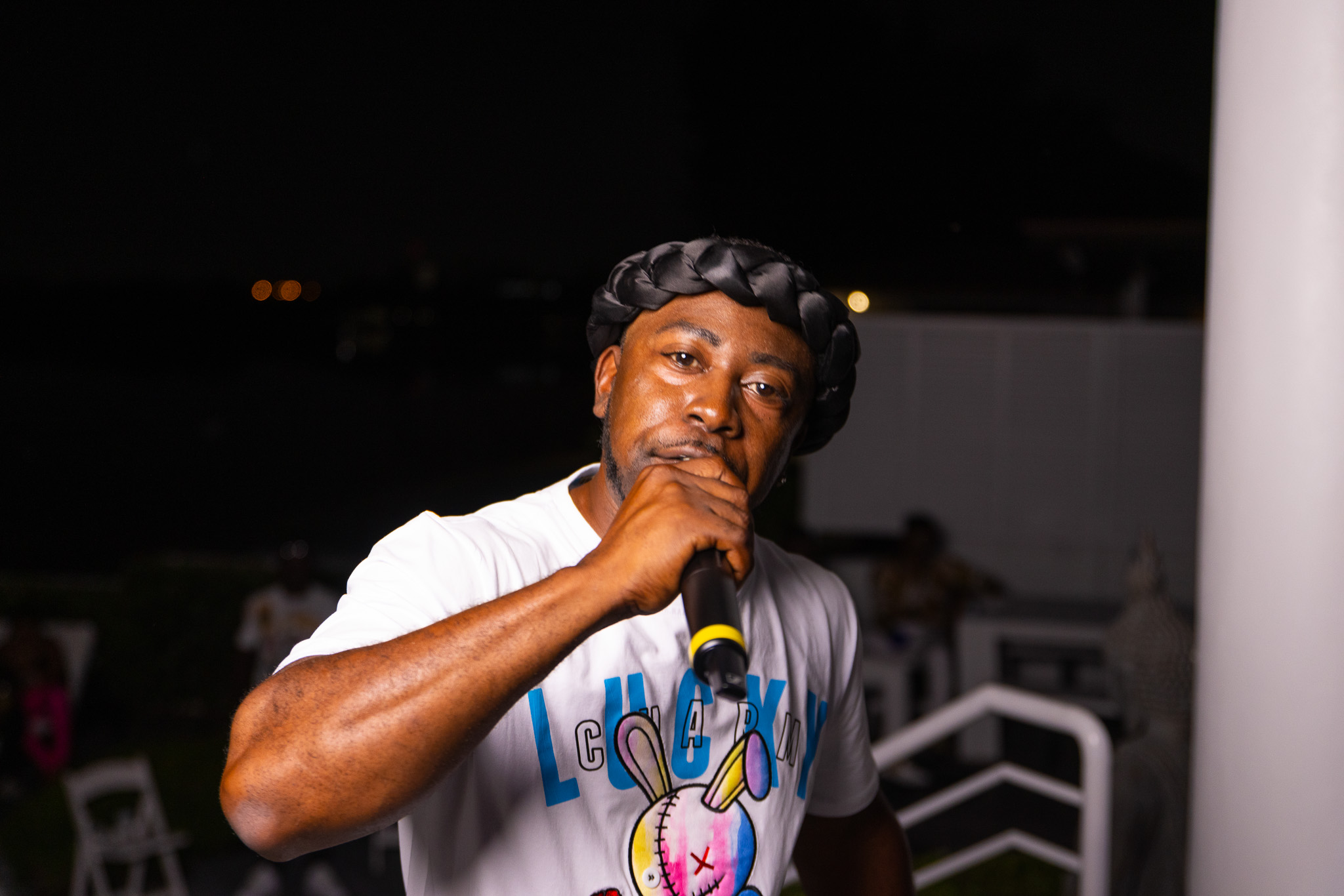 Jose Wrexx performing with a handheld microphone in a white graphic shirt.